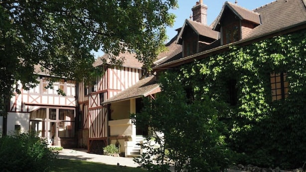 Une maison traditionnelle à colombages, dotée d’un jardin bien entretenu et d’une allée gravillonnée.