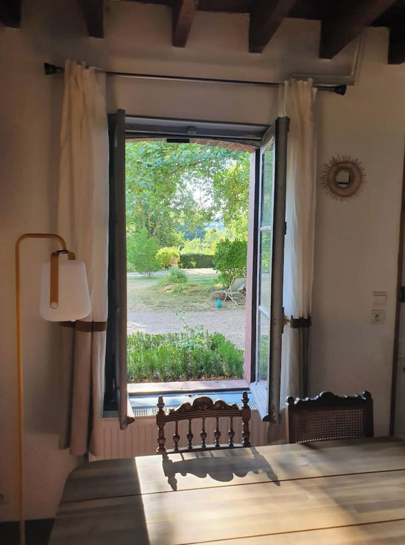 Une pièce avec un plancher en bois, un lit doté d’une tête de lit, une fenêtre avec des rideaux et une vue sur un jardin.