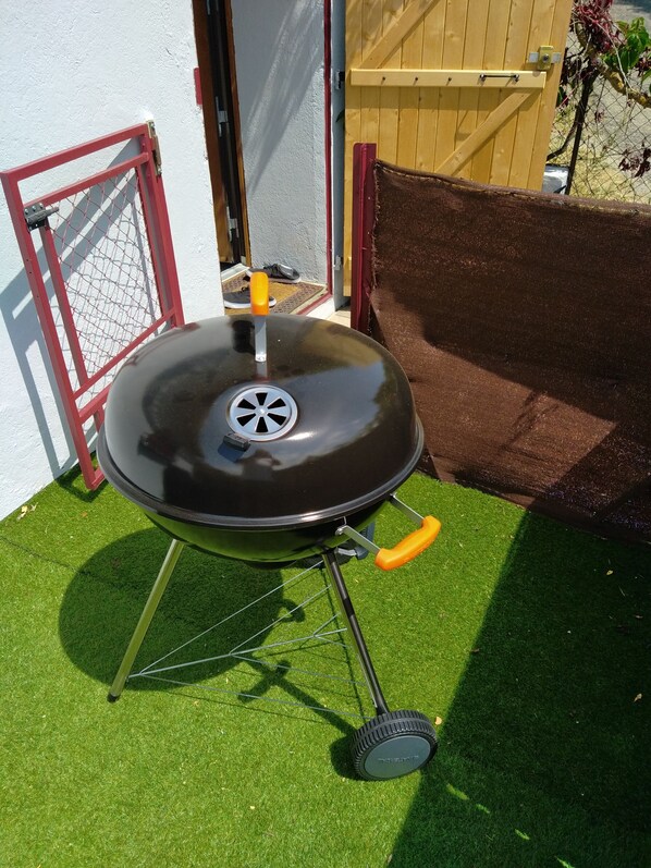 Un barbecue portable doté d’un couvercle noir et de poignées orange, posé sur du gazon synthétique.
