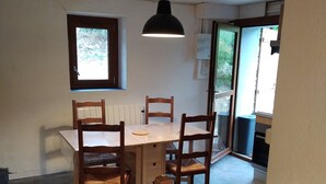 A dining area with a wooden table and chairs, a hanging light fixture, and a window with a view of greenery. - Maisonnette mountain view (Roquefeuil)