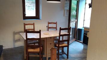 Un espace repas comprenant une table et des chaises en bois, un luminaire suspendu et une fenêtre donnant sur un paysage verdoyant.