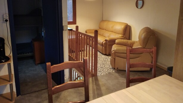 A living room with a sofa, two wooden chairs, a table, and a ceiling light. - Maisonnette mountain view (Roquefeuil)