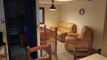 Un salon comprenant un canapé, deux fauteuils en bois, une table et un luminaire au plafond.