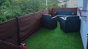 An outdoor patio with wicker furniture and a bottle of beer, surrounded by a brown fence and green artificial turf. - Maisonnette mountain view (Roquefeuil)