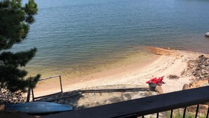 Udsigt over en sø med klart himmel, en sandstrand og en moler med en kano.