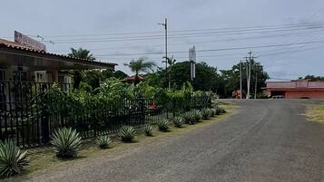 Una carretera con una valla y plantas a un lado, y edificios al otro.
