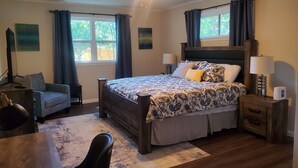 A bedroom with a large bed, two bedside tables with lamps, a chair, a desk, and a ceiling fan.