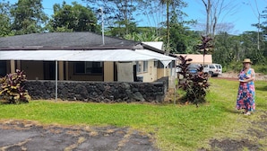 A house with a stone foundation, a covered porch, and a vehicle parked nearby.