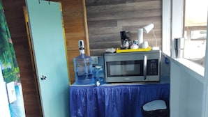 A compact kitchenette with a microwave, coffee maker, and water dispenser on a blue table.