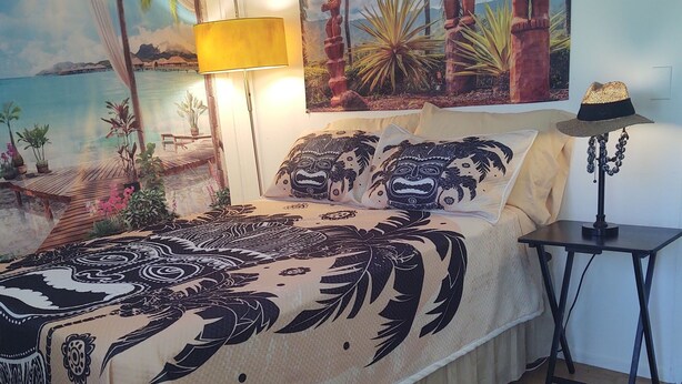 A bedroom with a bed, a nightstand, a lamp, and a painting of a tropical scene.