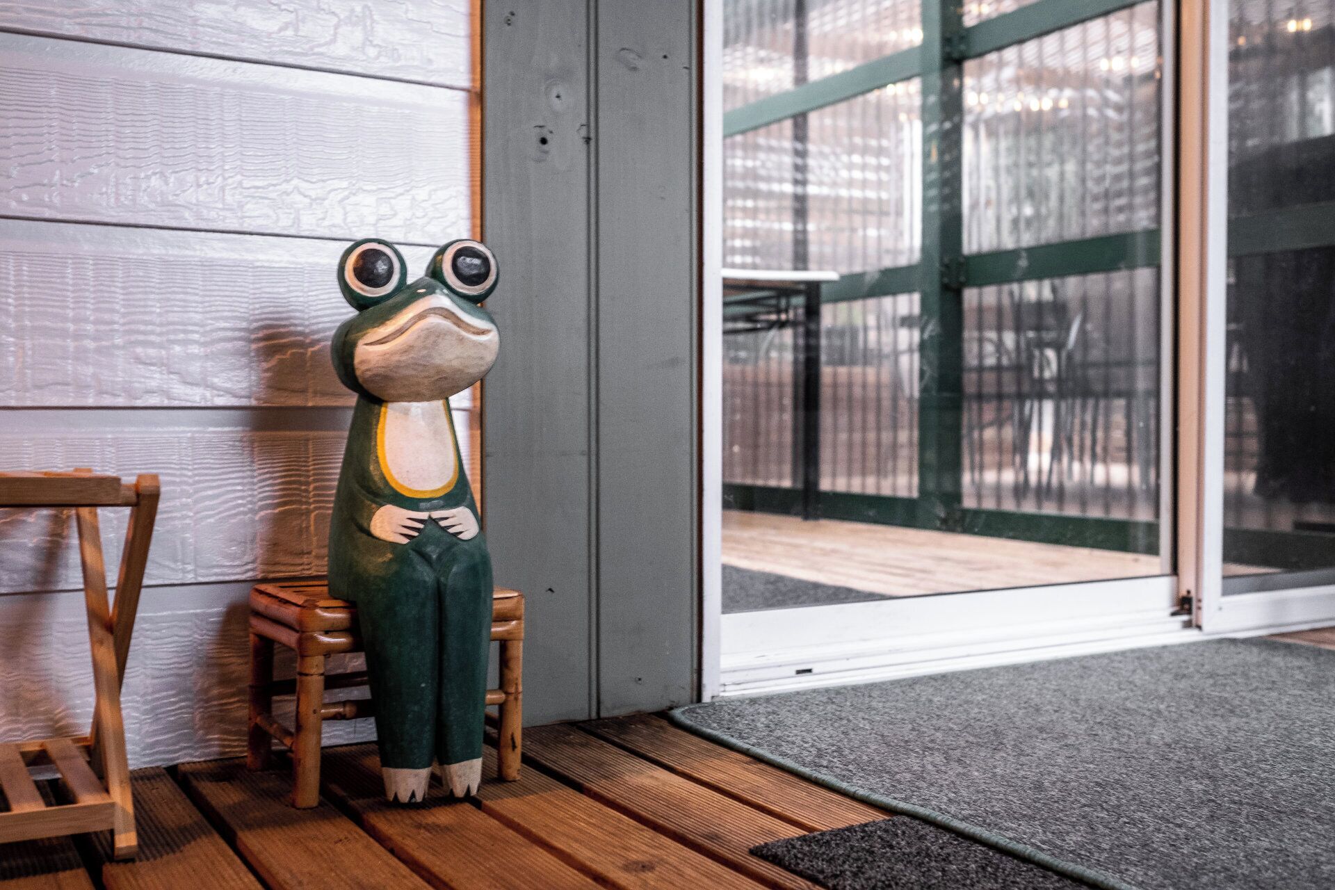 A frog-shaped sculpture on a wooden chair by a glass door.