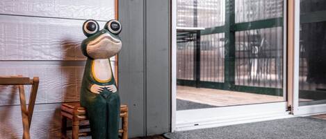 A frog-shaped sculpture on a wooden chair by a glass door.