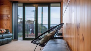 Ein modernes Interieur mit einem schwarzen Metallstuhl und einer Bank, Holzwänden und Blick durch Glastüren.