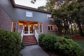 A two-story brick house with a front porch, a staircase leading to the entrance, and a well-maintained garden.