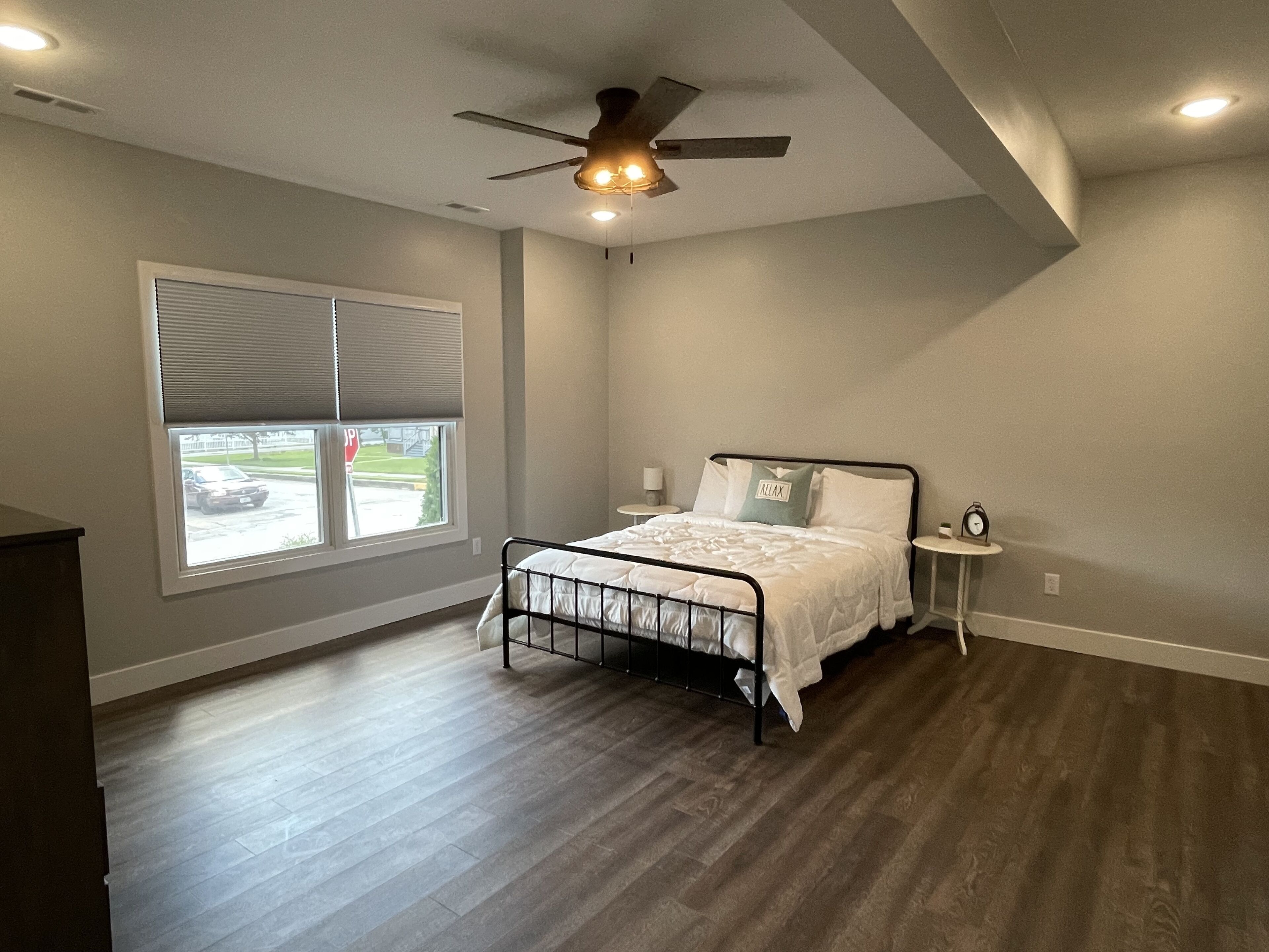 A bedroom with a bed, a ceiling fan, a window with blinds, and a view of the outside.