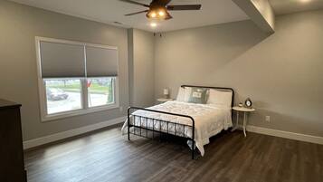 A bedroom with a bed, a ceiling fan, a window with blinds, and a view of the outside.