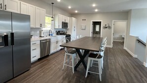 A modern kitchen with white cabinets, a stainless steel refrigerator, a dining table with chairs, and recessed ceiling lighting. - Historic Downtown Hermann Getaway-Walk to Wineries, Shops and Restaurants! (Hermann)