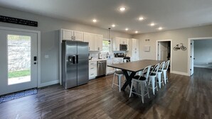 A modern kitchen with white cabinets, stainless steel appliances, and a wooden dining table. - Historic Downtown Hermann Getaway-Walk to Wineries, Shops and Restaurants! (Hermann)