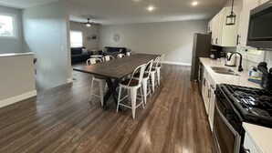 A modern kitchen with a dining area, wooden flooring, white cabinets, and a large window. - Historic Downtown Hermann Getaway-Walk to Wineries, Shops and Restaurants! (Hermann)