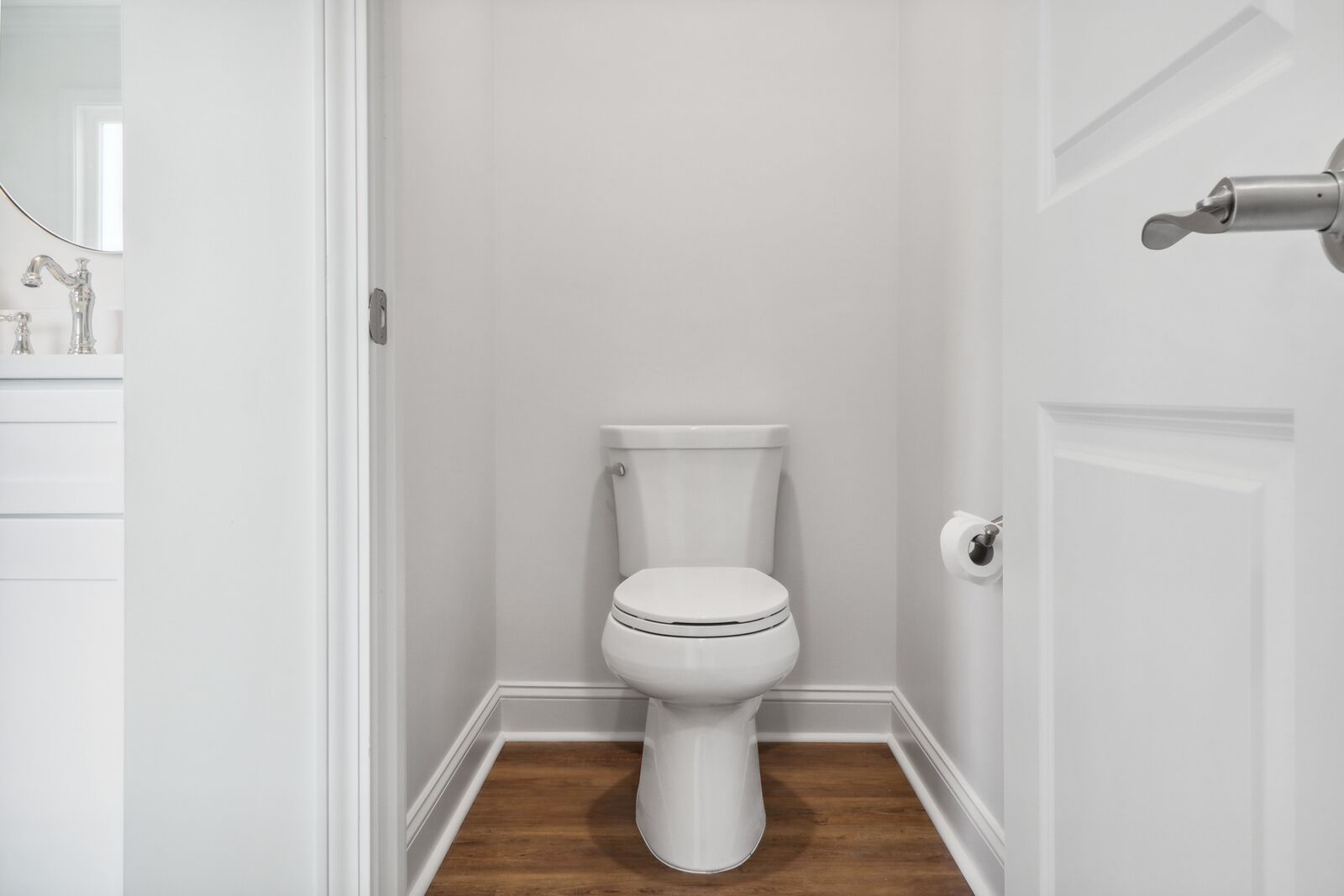 Een wit toilet in een badkamer met een houten vloer en witte wanden.