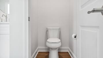 Een wit toilet in een badkamer met een houten vloer en witte wanden.