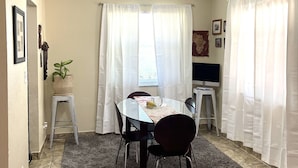 Un comedor con una mesa, sillas, una planta en maceta y cortinas.