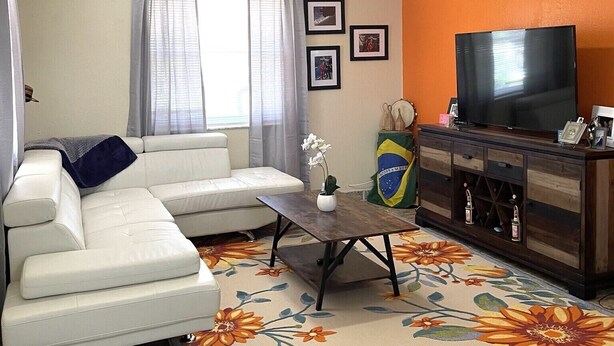 Una sala de estar con un sofá blanco, una mesa de centro de madera, un televisor y una bandera decorativa.