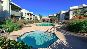 A pool area with lounge chairs, a pool, and a building with balconies.