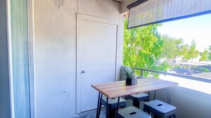 A balcony with a table and two chairs, a door, and a view of trees and parked cars.