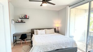 A bedroom with a bed, a desk, and a chair. There is a ceiling fan above the bed.