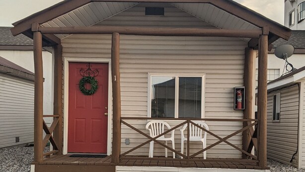 A single-story building with a red door, a porch with a railing, and a satellite dish.