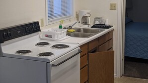 A compact kitchen with a stove, sink, and a clock on the wall.