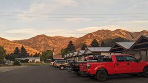 A row of cabins with a mountain backdrop, a red pickup truck parked in front, and a clear sky.