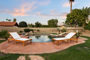 Un jardin à l’arrière de la maison avec une piscine, deux chaises longues et un jardin bien entretenu.