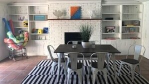 A dining area with a white brick fireplace, a black table, and white chairs. There are shelves with books and decorative items. - Welcome to the Sunshine Shack in Corpus Christi! (Corpus Christi)