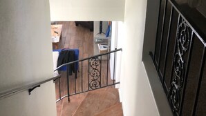 A staircase with a woven light fixture, a metal railing, and a view of a room with a bed and a table. - Welcome to the Sunshine Shack in Corpus Christi! (Corpus Christi)