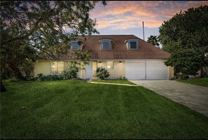 Stunning home with a brick facade, gabled roof, and dormer windows, set amidst a serene neighborhood with mature trees.