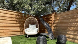 A backyard with artificial grass, a wicker chair, and two wicker ottomans. - Minutes to Lake Travis NEW Modern Townhome (Lago Vista)