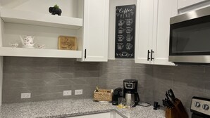 A modern kitchen with white cabinets, a granite countertop, a coffee maker, and a microwave. - Minutes to Lake Travis NEW Modern Townhome (Lago Vista)