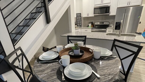 A modern kitchen with white cabinets, stainless steel appliances, and a dining area with a marble table and black chairs. - Minutes to Lake Travis NEW Modern Townhome (Lago Vista)