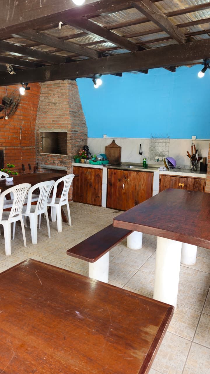 Una cocina al aire libre con horno de ladrillo, sillas de plástico blanco y una mesa de madera.