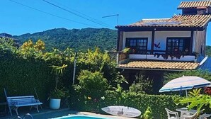 A swimming pool with lounge chairs and a table, surrounded by greenery and a house with a tiled roof. - Pousada Pouso do Marujo (Florianópolis)