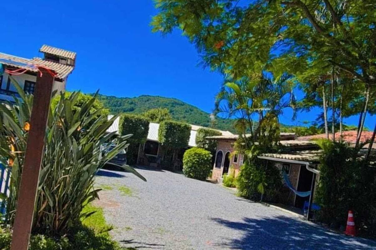 A paved pathway leading to a building with a tiled roof and arched windows, surrounded by lush greenery and a clear blue sky.