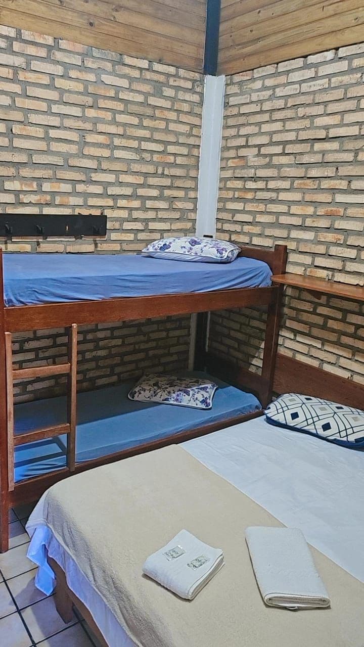 A bunk bed with a lower bunk and a separate bed below. There is a window with a black frame and a white curtain.