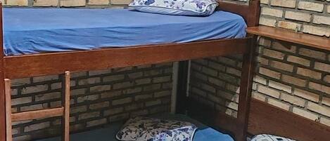 A bunk bed with a lower bunk and a separate bed below. There is a window with a black frame and a white curtain.