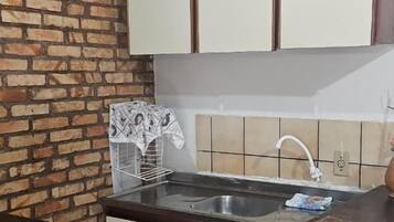 Una cocina con pared de ladrillo, armarios blancos, un lavamanos y un taburete pequeño.