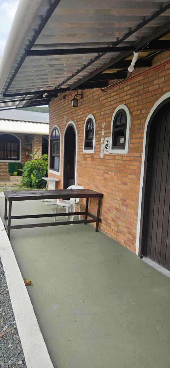 A covered outdoor area with a brick building, a metal table, and a white plastic chair.