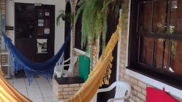 A covered outdoor area with a hammock, brick walls, and tiled flooring.