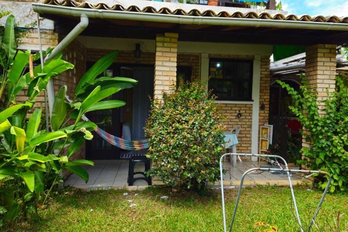 A house with a tiled roof, brick walls, a porch with a hammock, and various plants.