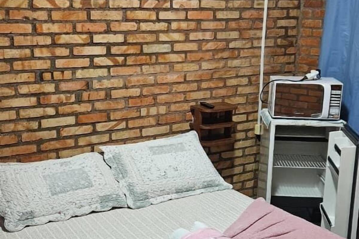 A room with a brick wall, a bed with a pink towel and white pillows, and a white air conditioning unit.